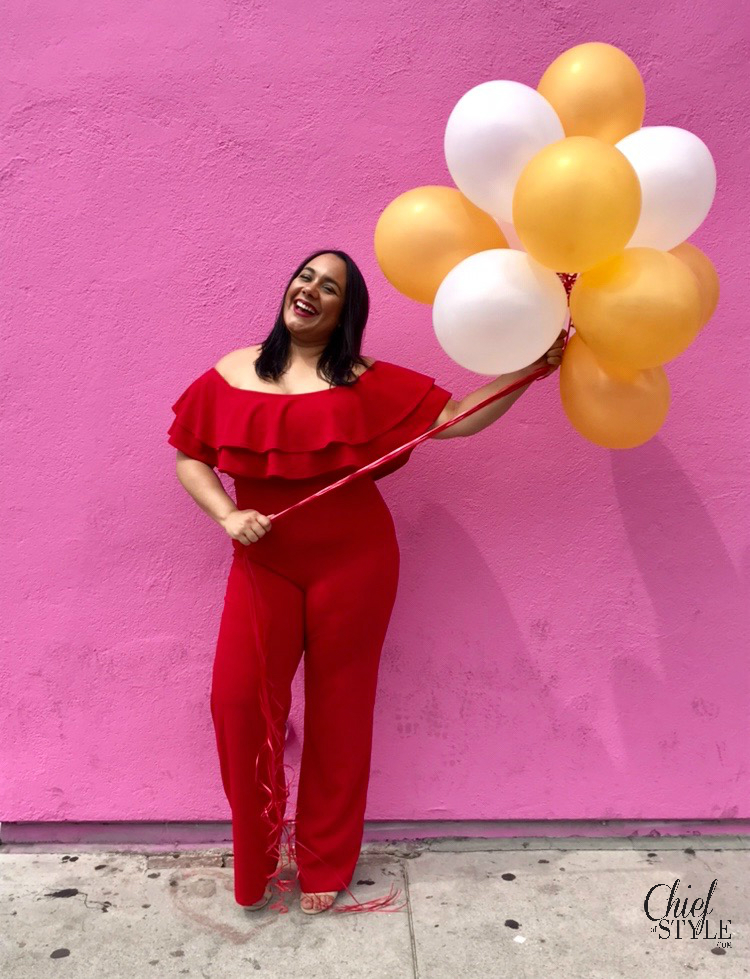 chief of style Amy Stretten in a birthday photo holding balloons in front of the Paul Smith wall on Melrose in a red plus size jumpsuit from fashion nova curve