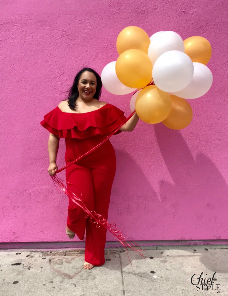 chief of style Amy Stretten in a birthday photo holding balloons in front of the Paul Smith wall on Melrose in a red plus size jumpsuit from fashion nova curve