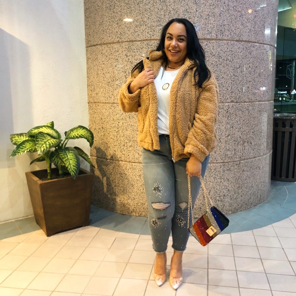 Plus size fashion blogger and journalist, Amy Stretten, aka The Chief of Style, wearing a teddybear coat, rhinestone embellished distressed skinny jeans from Lane Bryant, and clear heels while carrying a rhinestone encrusted rainbow purse in Sherman Oaks, California