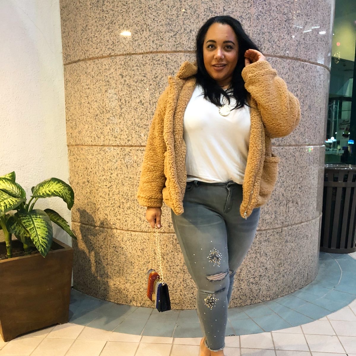 Plus size fashion blogger and journalist, Amy Stretten, aka The Chief of Style, wearing a teddybear coat, rhinestone embellished distressed skinny jeans from Lane Bryant, and clear heels while carrying a rhinestone encrusted rainbow purse in Sherman Oaks, California