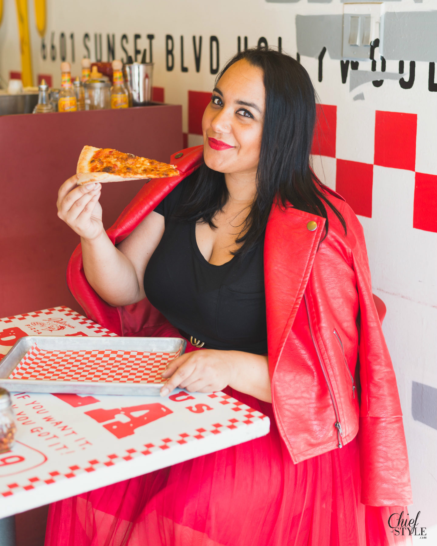 Amy Stretten Chief of Style at a pizza parlor in Hollywood, California wearing a red eloquii moto jacket and a red eloquii tuelle skirt